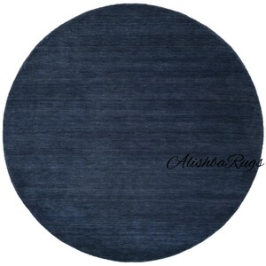 May include: A round, navy blue rug with a textured surface. The rug is a solid color and has a simple, modern design. The text "Alishba Rugs" is in the bottom right corner.