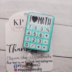 Peut inclure: Un porte-badge en forme de calculatrice bleu turquoise avec un cœur noir et le texte "I ♥ MATH". La calculatrice a des chiffres et des symboles noirs. Le porte-badge a un dos en plastique transparent et un clip en métal argenté.