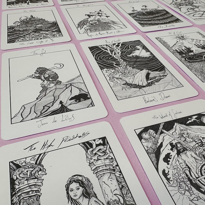 K&ouml;nnte beinhalten: Eine Sammlung von Tarotkarten mit detaillierten Schwarz-Wei&szlig;-Illustrationen. Jede Karte zeigt aufwendige Kunstwerke und handgeschriebene Titel, darunter "Der Narr", "Stab-Ass" und "Die Hohepriesterin". Die Karten liegen auf einer rosa Oberfl&auml;che.