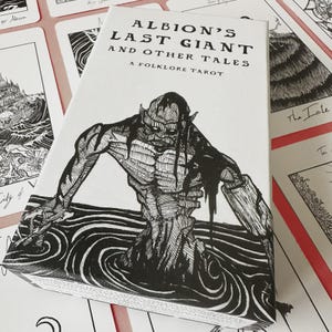 K&ouml;nnte beinhalten: Eine wei&szlig;e Tarotkartenbox mit dem Titel "Albion's Last Giant and Other Tales" und einem Folklore-Thema. Die Box zeigt eine Schwarz-Wei&szlig;-Illustration einer Kreatur, die aus dem Wasser auftaucht. Umgebende Karten sind sichtbar.