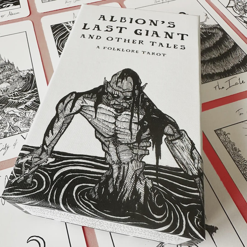K&ouml;nnte beinhalten: Eine wei&szlig;e Tarotkartenbox mit dem Titel "Albion's Last Giant and Other Tales" und einem Folklore-Thema. Die Box zeigt eine Schwarz-Wei&szlig;-Illustration einer Kreatur, die aus dem Wasser auftaucht. Umgebende Karten sind sichtbar.