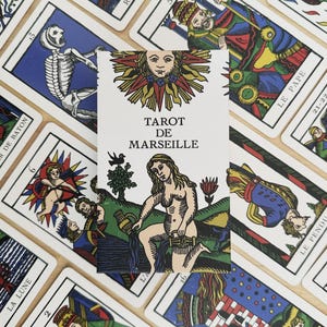 Könnte beinhalten: Eine Tarot de Marseille-Kartenschachtel mit einer zentralen Abbildung einer Figur, die Wasser aus zwei Gefäßen gießt, gekrönt von einem Sonnenmotiv. Die Schachtel ist von verschiedenen Tarotkarten mit farbenfrohen, detaillierten Darstellungen umgeben, darunter ein Skelett, ein König und eine hängende Figur.