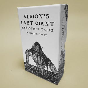 K&ouml;nnte beinhalten: Eine wei&szlig;e Tarotkartenbox mit dem Titel "Albion's Last Giant and Other Tales" in fetten schwarzen Buchstaben. Die Box zeigt eine Schwarz-Wei&szlig;-Illustration einer Kreatur. Die Worte "A Folklore Tarot" sind ebenfalls auf der Box aufgedruckt.