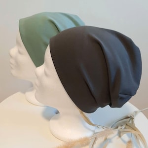 Könnte beinhalten: Zwei Stoff-Haarband, eines grün und eines schwarz, werden auf Mannequin-Köpfen präsentiert. Die Haarband sind aus einem weichen, dehnbaren Material gefertigt und haben ein schlichtes, klassisches Design.