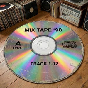 May include: A large, round rug designed to resemble a CD. The rug features the text "MIX TAPE '98", "A SIDE", and "TRACK 1-12". The rug has a holographic, rainbow-like appearance and is placed on a wooden floor. Other vintage audio equipment is visible.