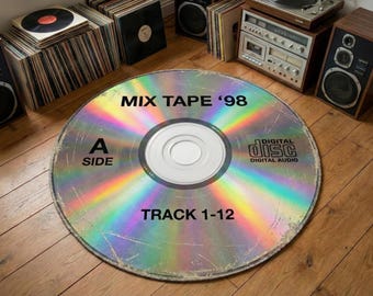 Op de afbeelding: Een groot, rond tapijt dat is ontworpen om op een cd te lijken. Het tapijt heeft de tekst "MIX TAPE '98", "A SIDE" en "TRACK 1-12". Het tapijt heeft een holografisch, regenboogachtig uiterlijk en ligt op een houten vloer. Andere vintage audioapparatuur is zichtbaar.