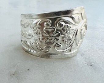 May include: A silver bracelet with a floral design. The bracelet is made of metal and has a smooth, polished finish.