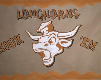Op de afbeelding: Een bruin-witte illustratie van een Longhorn-stier met de woorden "Longhorns" erboven en "Hook 'em" aan weerszijden. De afbeelding heeft een oranje rand en een bruine achtergrond.