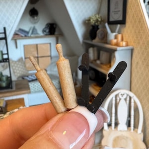 May include: A close-up of a hand holding two wooden rolling pins and two black ski-shaped objects. The rolling pins are made of natural wood and have a smooth finish. The ski-shaped objects are made of black plastic and have a textured surface.