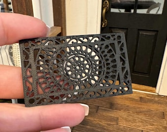 May include: A black, intricately designed, laser-cut metal doormat with a circular pattern in the centre.