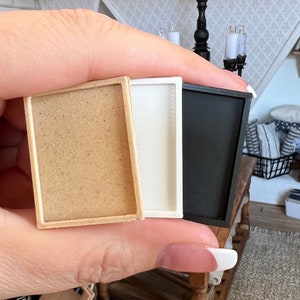 May include: Three miniature picture frames in different colours: natural wood, white, and black. The frames are all the same size and shape, and they are arranged side by side.