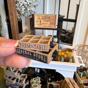 May include: Two miniature wooden crates stacked together. The top crate has six compartments and the text "FARM to TABLE" printed on the side. The bottom crate features a black label with the text "GENERAL STORE A.Y. ELLIS & CO EST. 1835" printed in white.