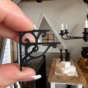 Könnte beinhalten: Schwarze Metall-Regalhalterung mit dekorativem Rollendesign. Die Halterung ist aus robustem Metall gefertigt und hat eine schwarze Oberfläche.