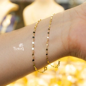 May include: A delicate gold bracelet with a repeating pattern of small, rectangular links. The bracelet is worn on a wrist, showcasing its subtle design and shine. The bracelet is a piece of jewelry.