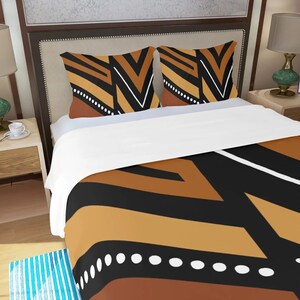 May include: Bedding set with a duvet cover and two pillowcases. The design features a geometric pattern in black, brown, white, and tan. The bed has a white sheet and is set against a neutral-toned headboard.