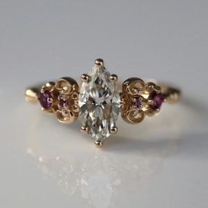 Op de afbeelding: Een gouden ring met een grote, marquise-vormige diamant en twee kleinere roze edelstenen aan weerszijden.