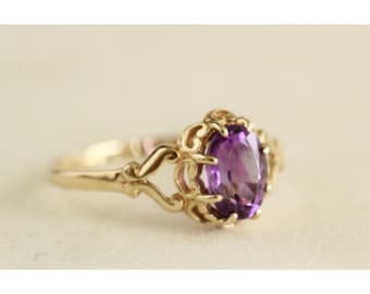 Puede incluir: Un anillo de oro con una amatista ovalada engastada en un diseño delicado y ornamentado.