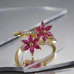 Op de afbeelding: Gouden ring met twee roze bloemmotieven bezet met heldere stenen.
