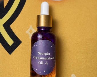 May include: A glass dropper bottle with a gold-colored cap and a white dropper tip. The bottle contains a golden liquid and has a purple oval label with white text that reads Scorpio Transmutation Oil and a small scorpion icon.