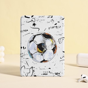 May include: White rectangular phone case featuring a soccer ball illustration with black and gold accents. The case has a scribbled background with various black markings. A pair of white wireless earbuds and a charging case are also visible.