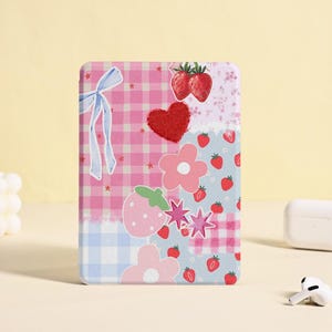 Puede incluir: Una funda para teléfono de color rosa y azul con un diseño de patchwork que incluye fresas, flores, estrellas y un corazón.