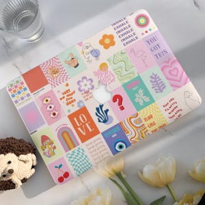 May include: A colorful laptop case with a collage of graphics and text. The design includes flowers, hearts, and the words "INHALE EXHALE" and "YOU GOT THIS." The case has a cutout for the Apple logo.