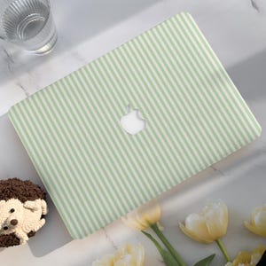 May include: A laptop with a light green and white striped design. The laptop has a cut-out apple logo. A glass of water, a hedgehog-shaped pastry, and yellow tulips are also in the image.