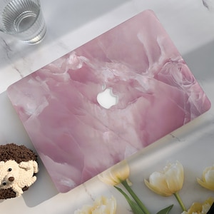 以下が含まれることがあります： 白いアップルロゴが付いたピンクの大理石のラップトップスキン。スキンは薄いピンクと白の大理石模様です。