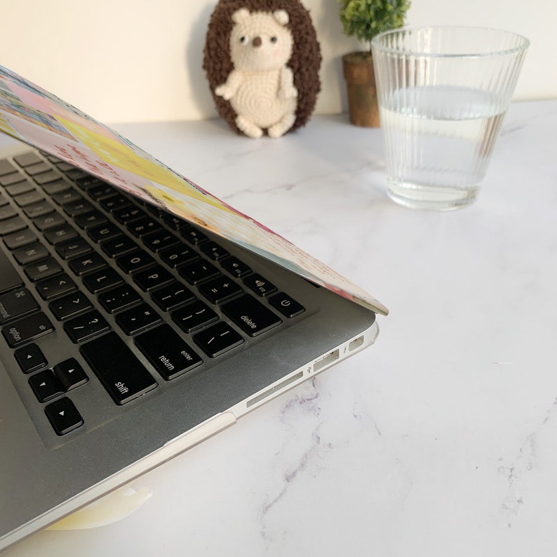 May include: A silver laptop computer with a colorful patterned case. The laptop is open and the keyboard is visible. The laptop is sitting on a white marble surface.
