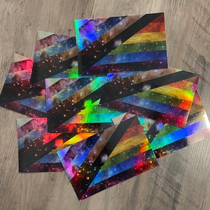 May include: A stack of rainbow pride flags with a galaxy print. The flags are made of a holographic material that shimmers in the light.