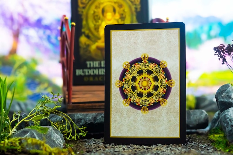 May include: A tarot card with a gold and purple wheel design, set against a neutral background. The card is framed in black. The image also features a bridge and a book with gold lettering, suggesting a spiritual or divination theme.