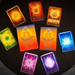 May include: A set of chakra insight oracle cards with a guidebook. The cards feature colorful illustrations of chakras with the name of each chakra printed below. The guidebook is orange with a picture of a person meditating with chakras.