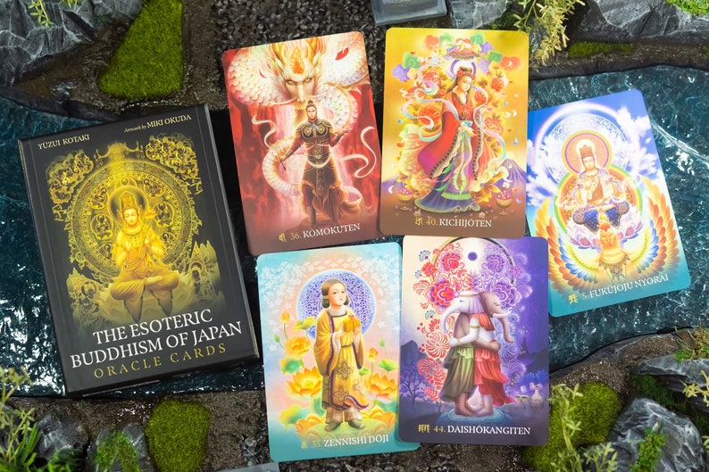 May include: A deck of "The Esoteric Buddhism of Japan Oracle Cards" with a black box featuring gold lettering and illustrations. Several colorful oracle cards are displayed, each with unique artwork and Japanese text. The cards depict various figures and symbols.