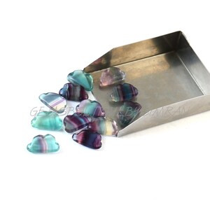 May include: A collection of small, cloud-shaped, multi-colored fluorite gemstones. The gemstones are a mix of purple, blue, and green.