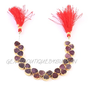 May include: A purple gemstone necklace with gold accents and red tassels. The necklace is made of irregular shaped stones and is strung on a silver cord.