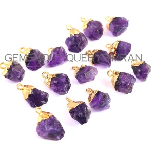 Könnte beinhalten: Eine Sammlung von 12 Amethyst-Kristallanhängern mit vergoldeter Öse. Die Amethystkristalle sind roh und haben eine natürliche, unregelmäßige Form. Die Anhänger sind perfekt für die Schmuckherstellung oder das Basteln.
