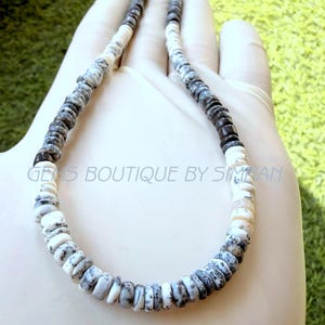 May include: A necklace composed of small, disc-shaped beads in alternating patterns of solid white and mottled gray and black. The beads are strung in a circular arrangement, featuring a repeating color sequence throughout the entire length of the strand.