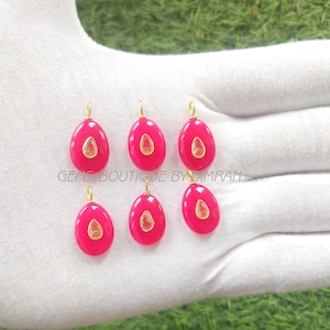 May include: Six oval pink pendants with gold-coloured bails and a central, lighter-coloured oval stone. The pendants are displayed on a white surface, with the text "GEMS BOUTIQUE BY DIMRAN" visible.