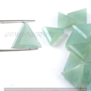Op de afbeelding: Een groep lichtgroene driehoekige edelsteen cabochons. De cabochons zijn gefacetteerd en hebben een gladde, gepolijste afwerking. De cabochons zijn willekeurig gerangschikt op een wit oppervlak.