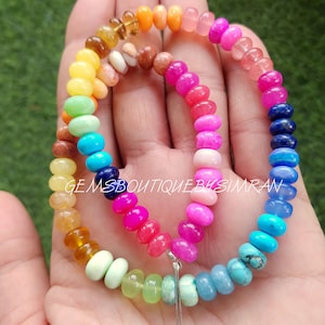 Puede incluir: Un collar de cuentas de colores con un arcoíris de piedras preciosas. El collar presenta una variedad de colores, incluyendo amarillo, naranja, rosa, azul y verde. El texto "GEMSBOUTIQUEBYSIMRAN" es visible.