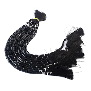 Può includere: Una collana di perle di onice nero con forma rettangolare sfaccettata. Le perle sono infilate su un cordoncino con nappe nere all'estremità.