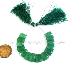 Puede incluir: Una hebra de 10 cuentas de piedras preciosas verdes con forma cuadrada facetada. Las cuentas están enhebradas en un alambre plateado con detalles de borlas verdes en cada extremo. Las cuentas miden aproximadamente 2,5 cm.