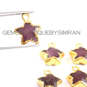 May include: Five gold-plated star-shaped charms with a deep pink ruby gemstone in the center. The charms have a loop at the top for attaching to jewelry.