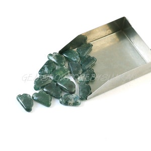 Könnte beinhalten: Eine Sammlung grüner Achat-Edelsteine ​​in Wolkenform in einer Metallschaufel. Die Perlen sind grün gemustert mit weißen und grauen Markierungen.