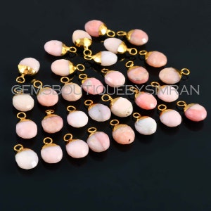 May include: A collection of 25 pink opal gemstone pendants with gold-plated jump rings. The opals are a mix of light and dark pink hues, and the jump rings are a shiny gold colour.