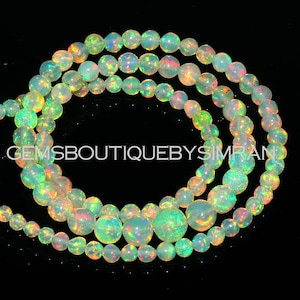 May include: A strand of iridescent opal beads in various shades of green, yellow, and pink. The beads are round and have a smooth, polished finish.