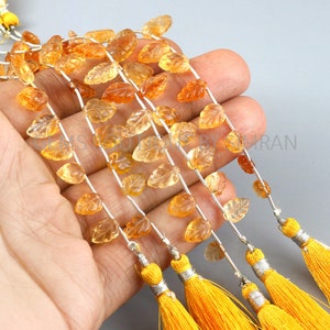 Può includere: Una collana di perle di pietra preziosa arancione intagliate a forma di foglie. Le perle sono infilate su un filo d'argento e hanno nappe gialle alle estremità.