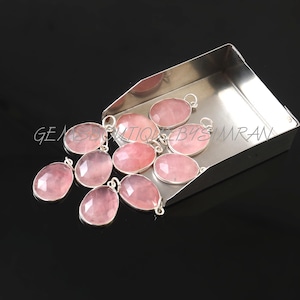 Könnte beinhalten: Zehn rosafarbene Rosenquarz-Anhänger mit silbernen Ösen. Die Anhänger liegen auf einem silbernen Tablett.