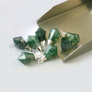 May include: A group of seven green agate gemstone pendants with silver jump rings. The pendants are in the shape of a teardrop with a faceted point. The pendants are scattered on a silver surface.