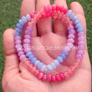 Puede incluir: Una hebra de cuentas de piedras preciosas de color rosa, morado y azul. Las cuentas son redondas y tienen un acabado liso y pulido. Las cuentas están enhebradas en un hilo fino y plateado.